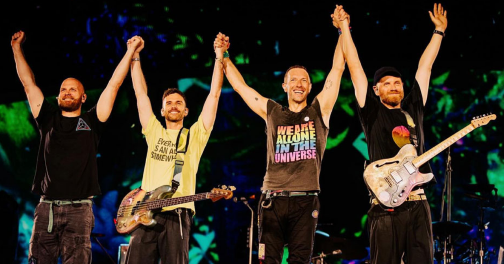 Integrantes da banda Coldplay de mãos dadas no palco.