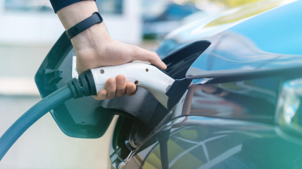 Homem conectando carregador em um carro elétrico na estação de carga