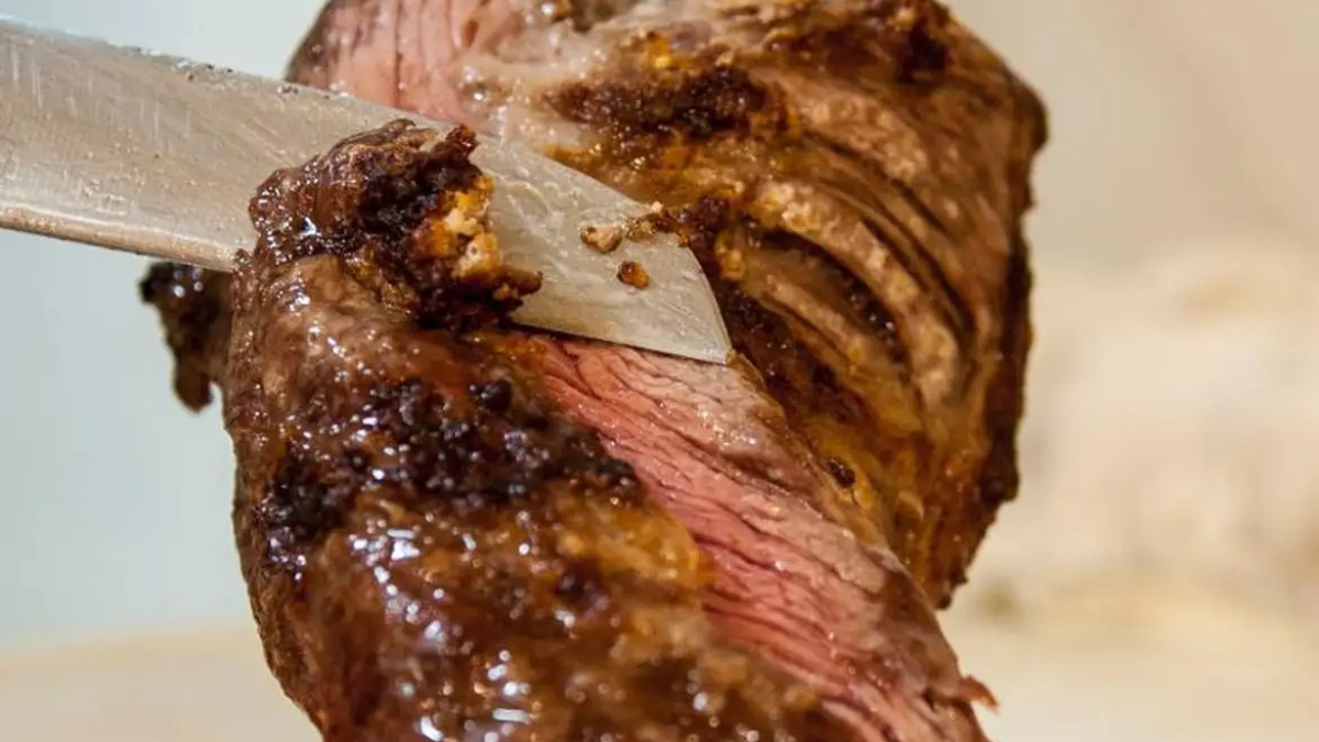 foto mostra peça de carne sendo cortada em churrasco