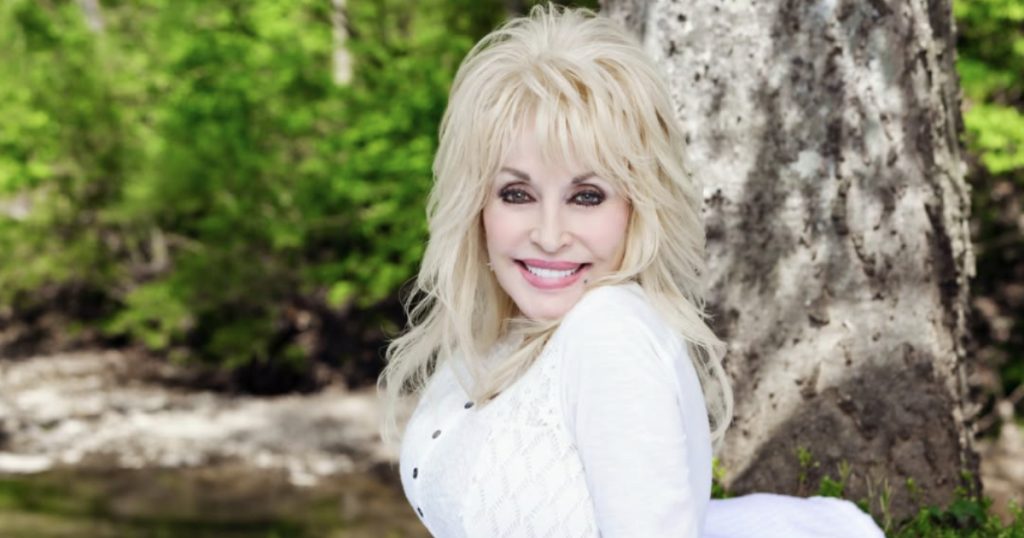 dolly parton sentada em um lugar com árvores e vestindo uma roupa branca