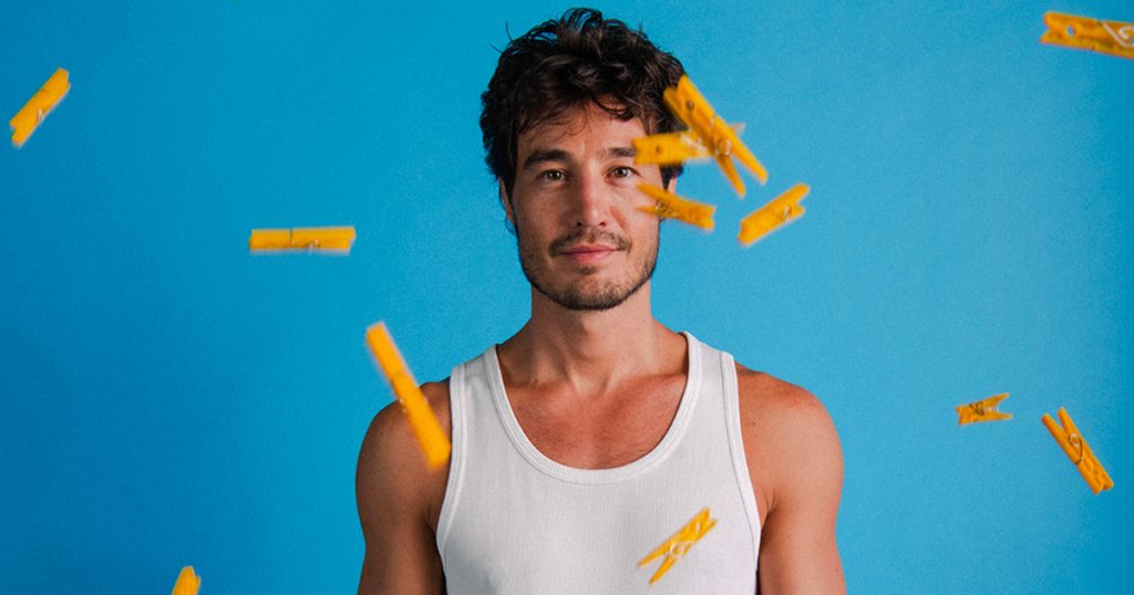 tiago iorc com uma camiseta branca em um fundo azul e vários pregadores voando