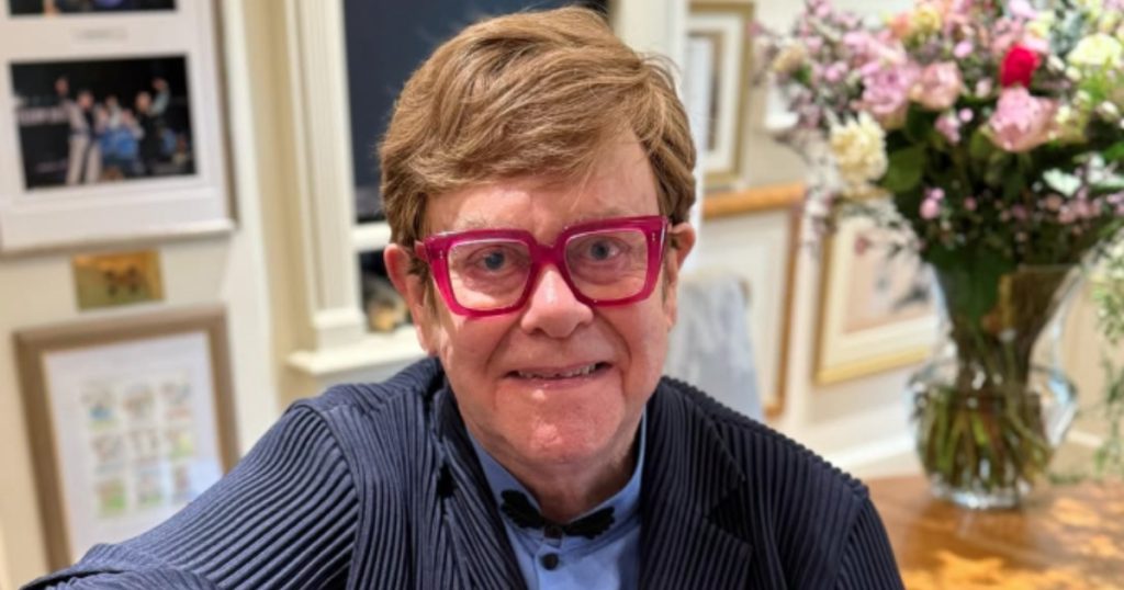 elton john sentado em uma cadeira e sorrindo