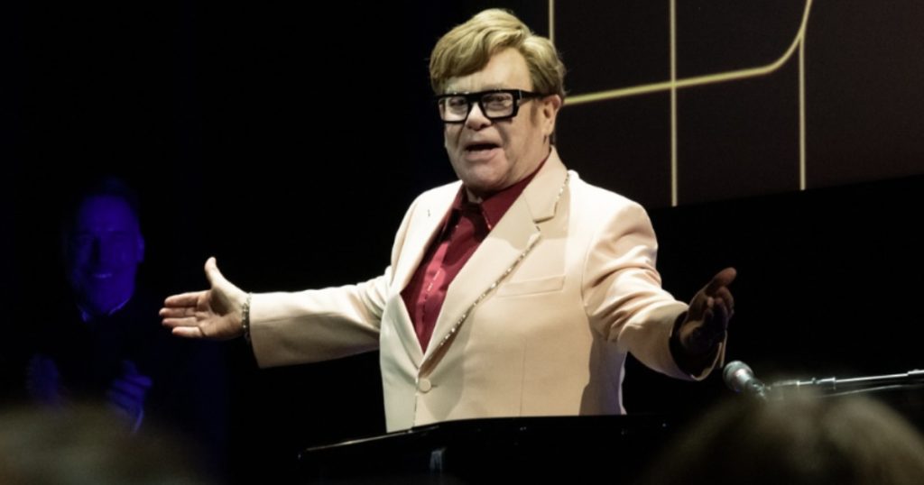 elton john de braços abertos e usando terno