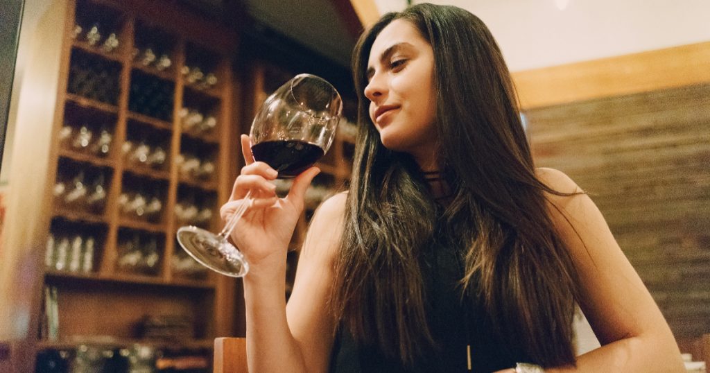 pessoa tomando taça de vinho em uma adega